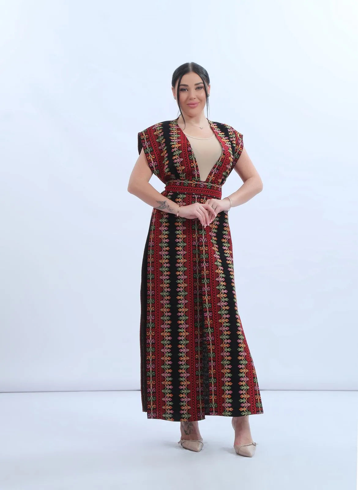 Model wearing a fully embroidered sleeveless Levantine bisht in black chiffon with red and multicolor Tatreez-inspired embroidery, عارضة ترتدي بشت نسائي شامي مطرز بالكامل من الشيفون الأسود بتطريز تراثي متعدد الألوان.