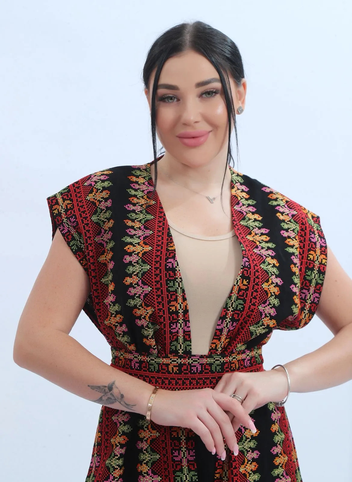 Model wearing a fully embroidered sleeveless Levantine bisht in black chiffon with red and multicolor Tatreez-inspired embroidery, عارضة ترتدي بشت نسائي شامي مطرز بالكامل من الشيفون الأسود بتطريز تراثي متعدد الألوان.