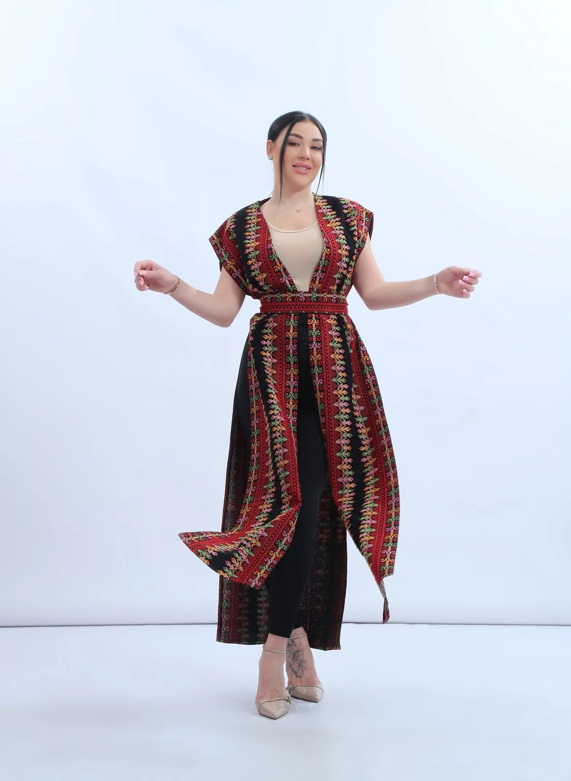 Model wearing a fully embroidered sleeveless Levantine bisht in black chiffon with red and multicolor Tatreez-inspired embroidery, عارضة ترتدي بشت نسائي شامي مطرز بالكامل من الشيفون الأسود بتطريز تراثي متعدد الألوان.