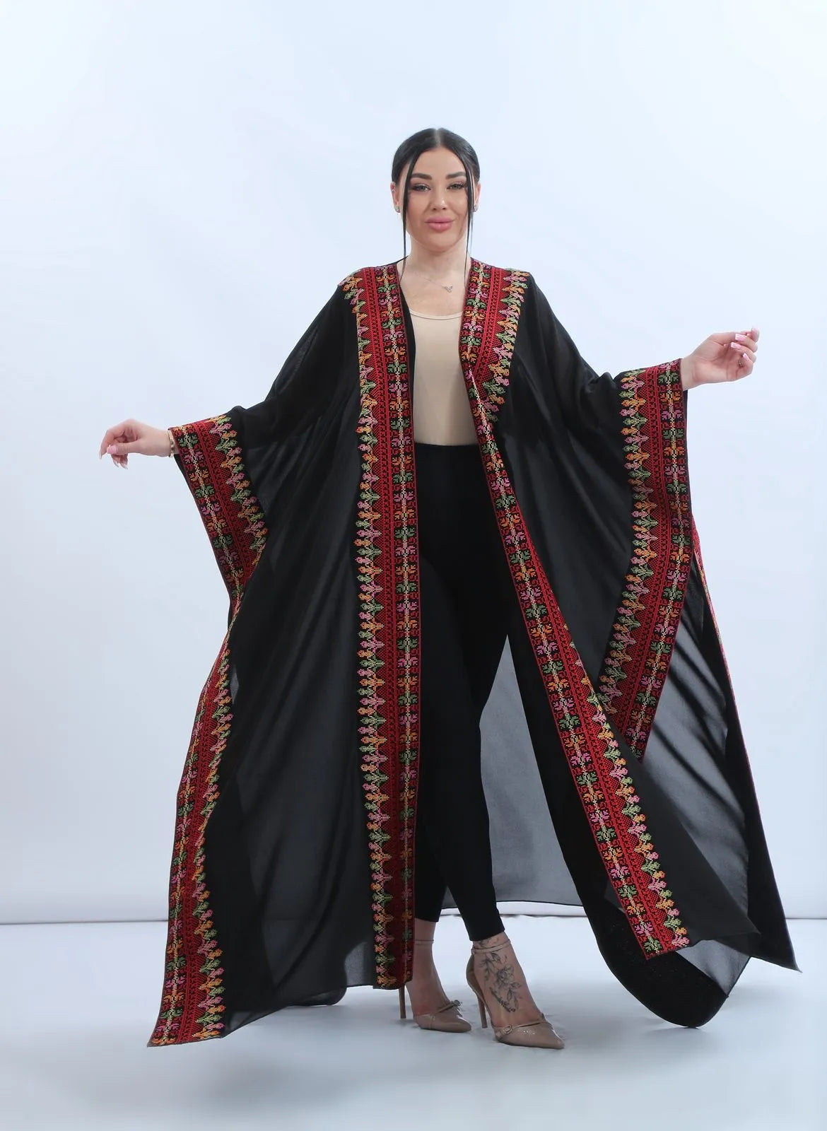 Model wearing a Khaleeji style black chiffon bisht held open to show the full multicolor Levantine embroidered panels and wide sleeves, عارضة ترتدي بشت شامي أسود من الشيفون بتصميم خليجي مفتوح يظهر التطريز التراثي متعدد الألوان والأكمام الواسعة