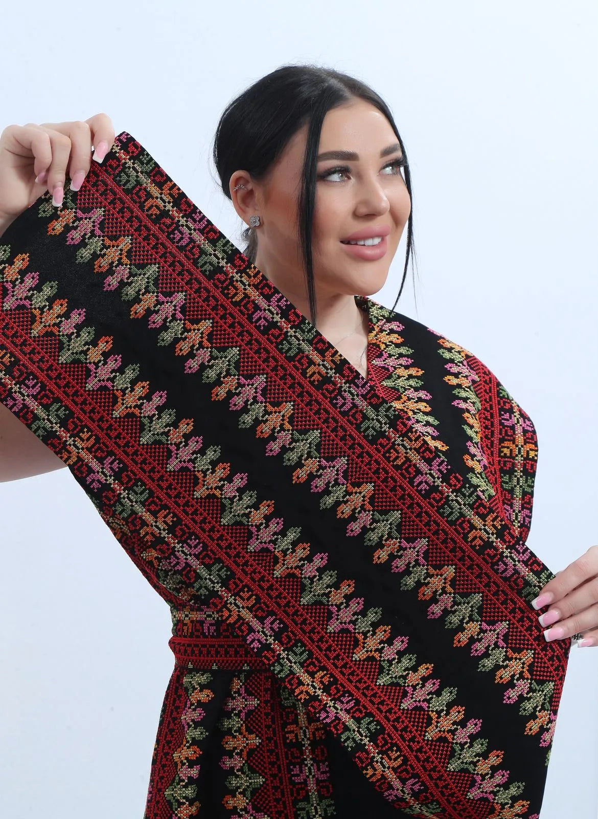 Model holding up the embroidered edge of the bisht to show the density of the cross-stitch floral motifs, عارضة ترفع حافة البشت المطرزة لإظهار كثافة نقوش التطريز الزهرية بغرزة الصليب
