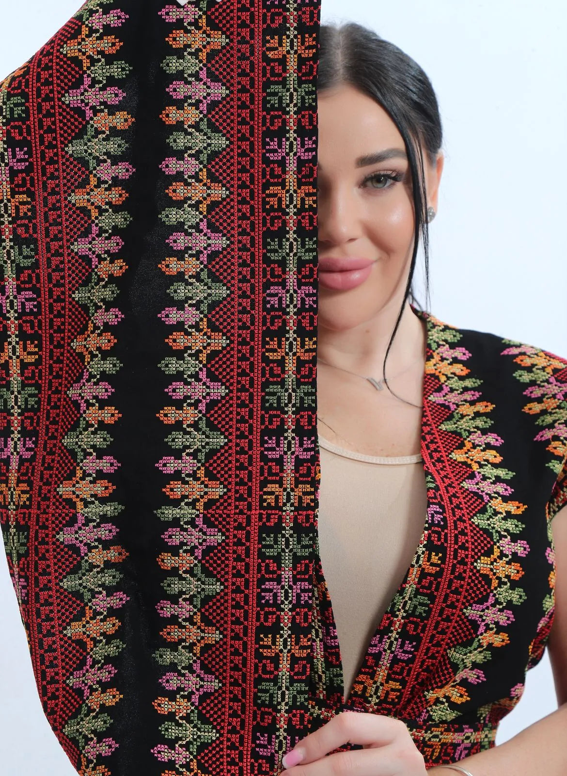 Close-up of the Levantine Tatreez-inspired embroidery on the black chiffon bisht in deep red, olive green, rose pink and apricot, لقطة قريبة للتطريز الشامي على البشت الأسود من الشيفون بدرجات الأحمر الغامق والأخضر الزيتوني والوردي والمشمشي